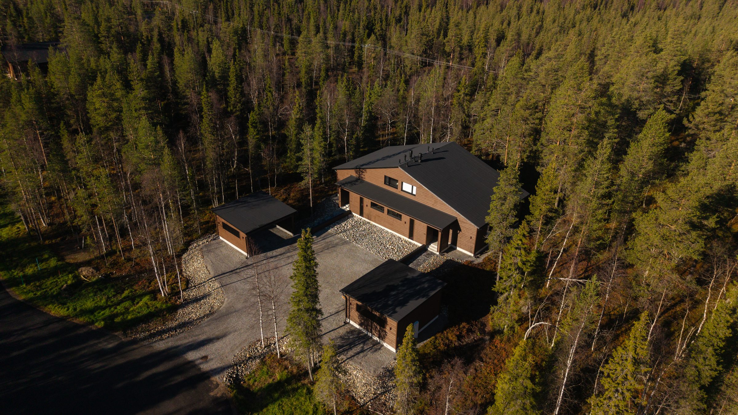 Villa Löhö from the air on a clear autumn day: the drive running up between two carports to a dark timber building, forest on every side.