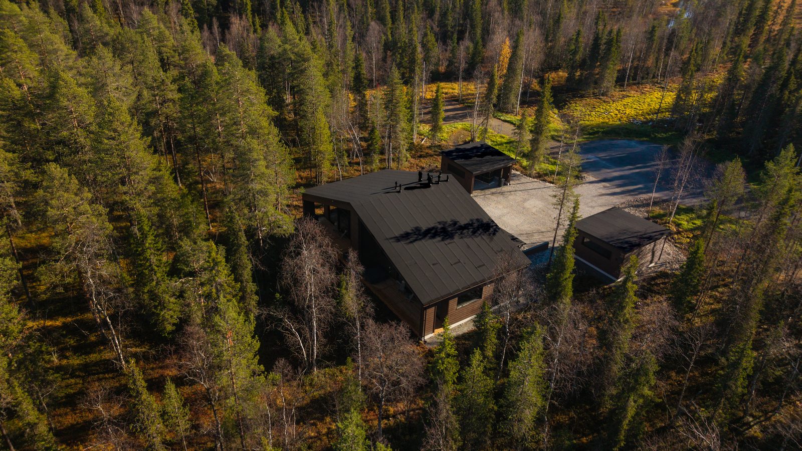 Villa Löhö from above and behind: one long building with two entrances, an open two-car carport on each side and a wide gravel yard between them.