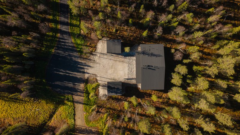Villa Löhö almost directly from above, showing the roofline, the gravel yard and the surrounding forest in autumn colour.
