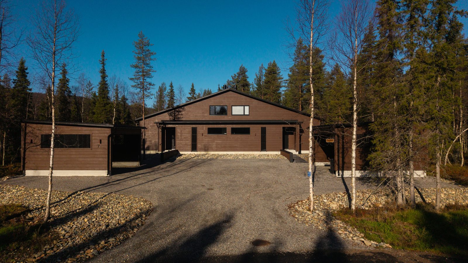 The front of Villa Löhö on a clear autumn day: dark timber cladding, black roof, two covered entrances and an open carport on each side of the yard.