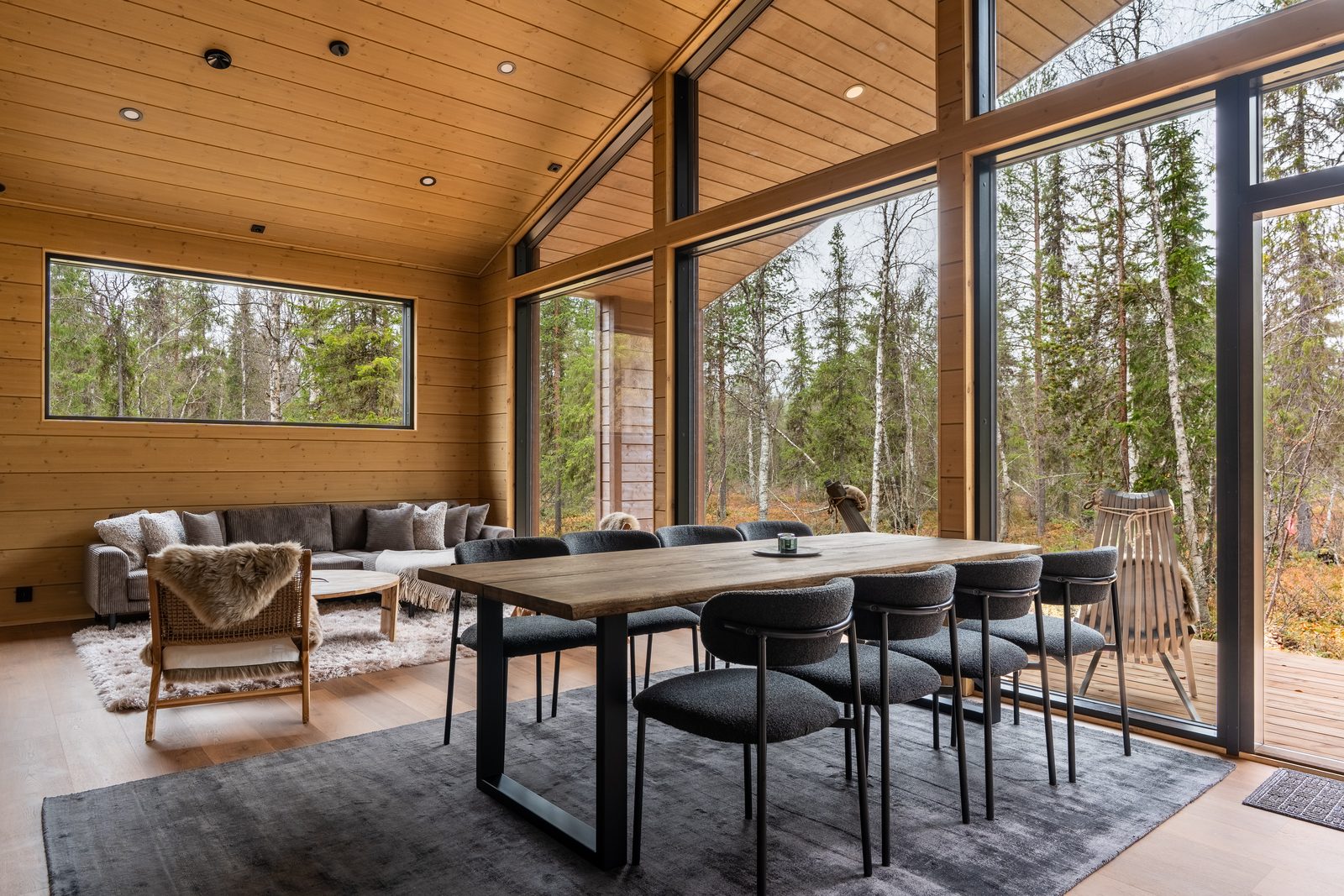 The open living and dining room: timber walls, a vaulted ceiling and a full-height window wall onto the covered deck.