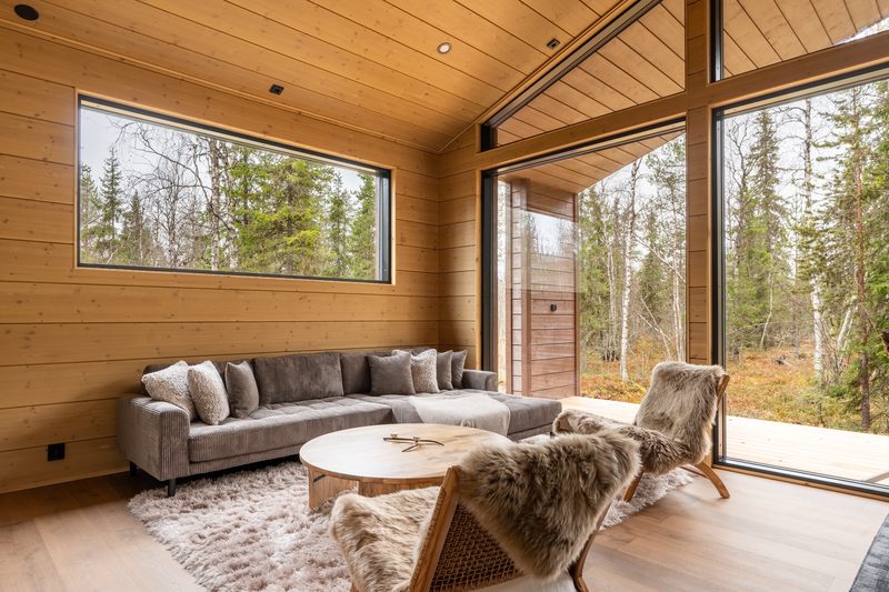 A deep grey sofa and two fur-draped chairs around a round wooden table, with windows on two sides.