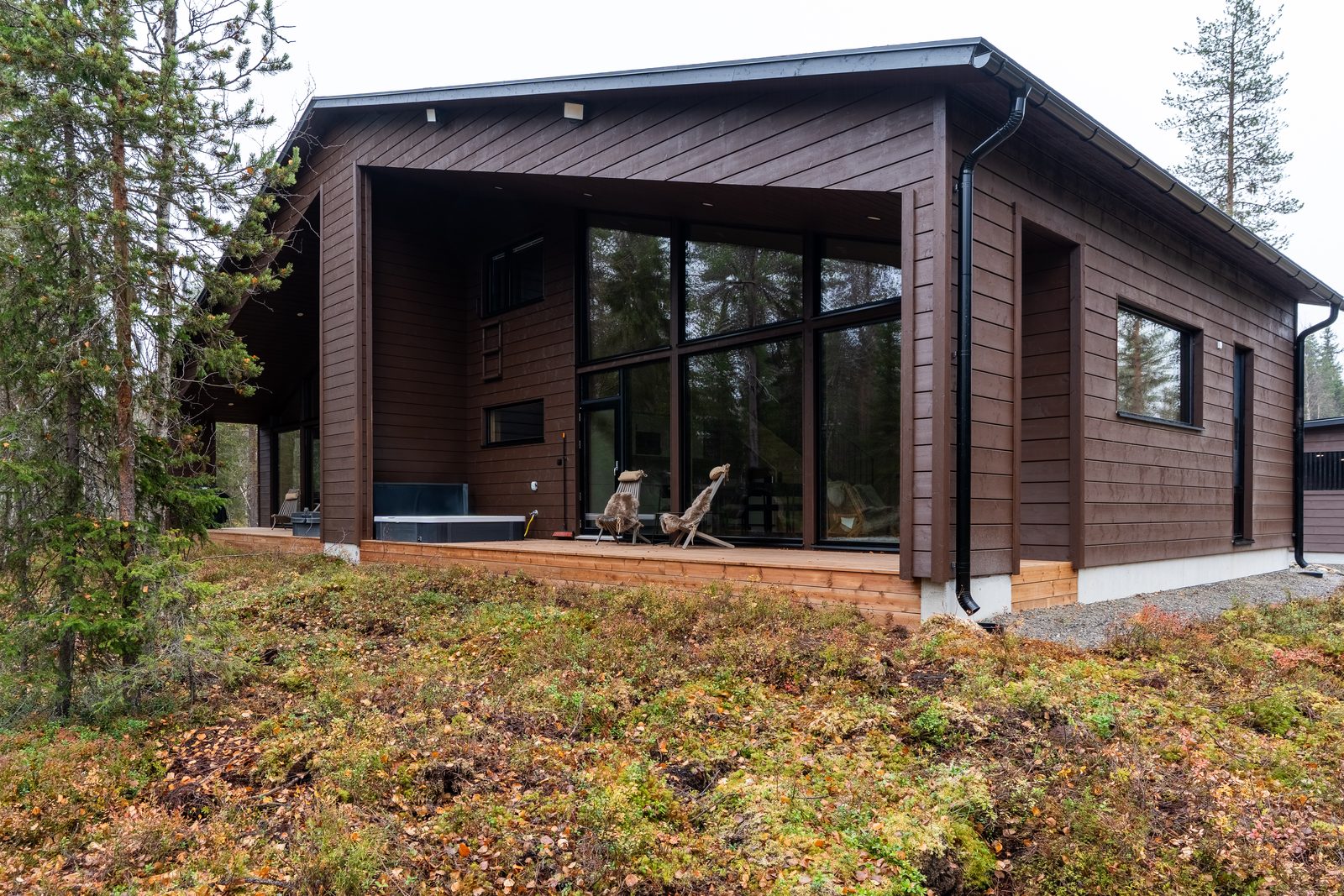 The back of Villa Löhö: a long covered deck with a jacuzzi and chairs, facing open forest.