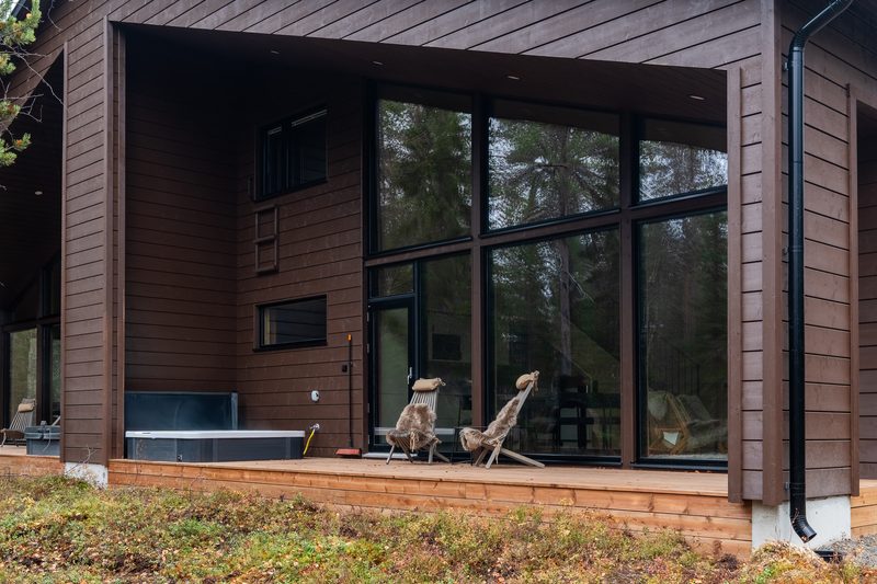 The covered deck from the side, with the jacuzzi, fur-draped chairs and a stack of firewood.