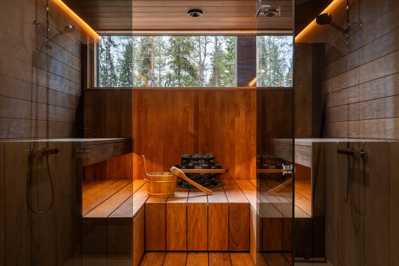 The sauna seen through its glass wall, the electric heater piled with stones and the benches lit from above.