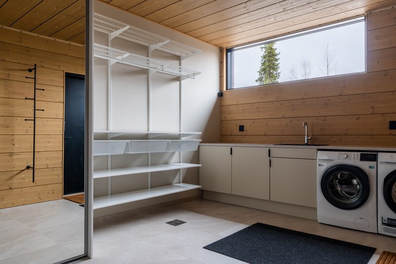 The utility room with a washing machine and tumble dryer side by side, open shelving, a laundry sink and a door outside.