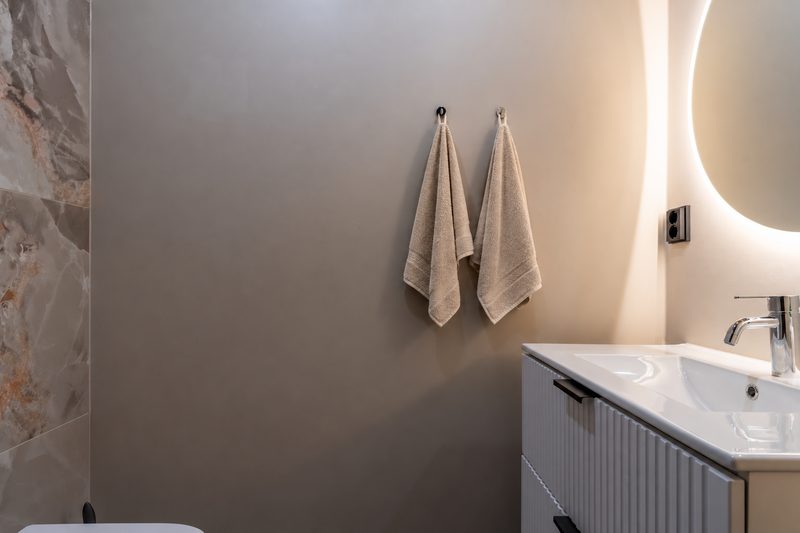 A WC detail: two folded towels on hooks beside the backlit round mirror.
